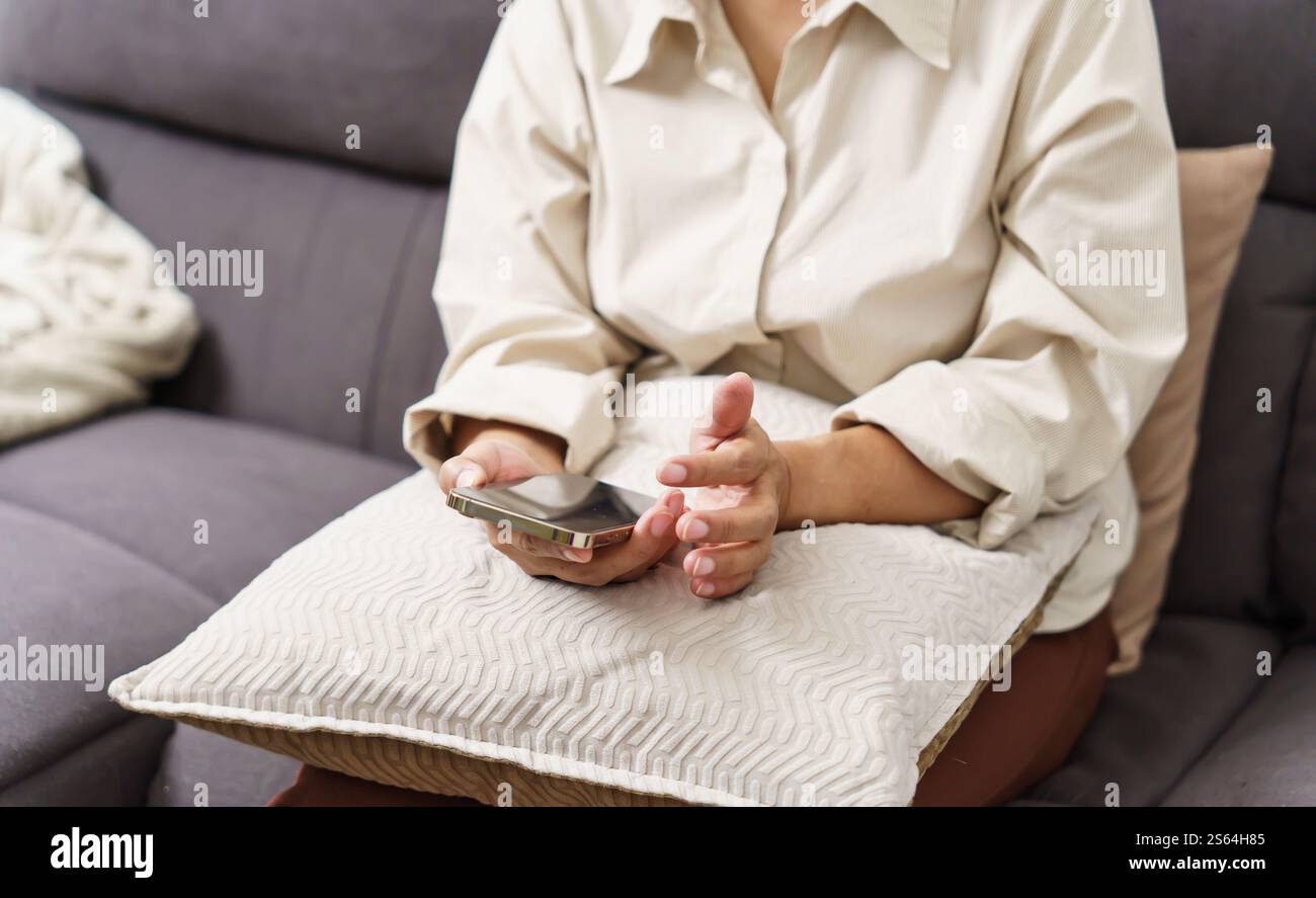 Donna asiatica di mezza età che tiene il telefono cellulare. donna anziana con smartphone. donna anziana che utilizza lo smartphone a casa con il concetto di tecnologia. Foto Stock