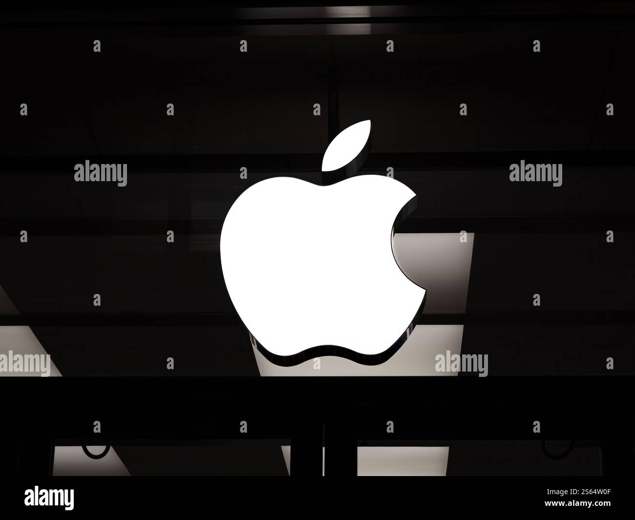 Basilea, Svizzera - 23 dicembre 2024: Il logo Apple si illumina su una facciata oscurata dell'Apple Store - lo scatto notturno minimalista sottolinea l'ae moderno del marchio Foto Stock