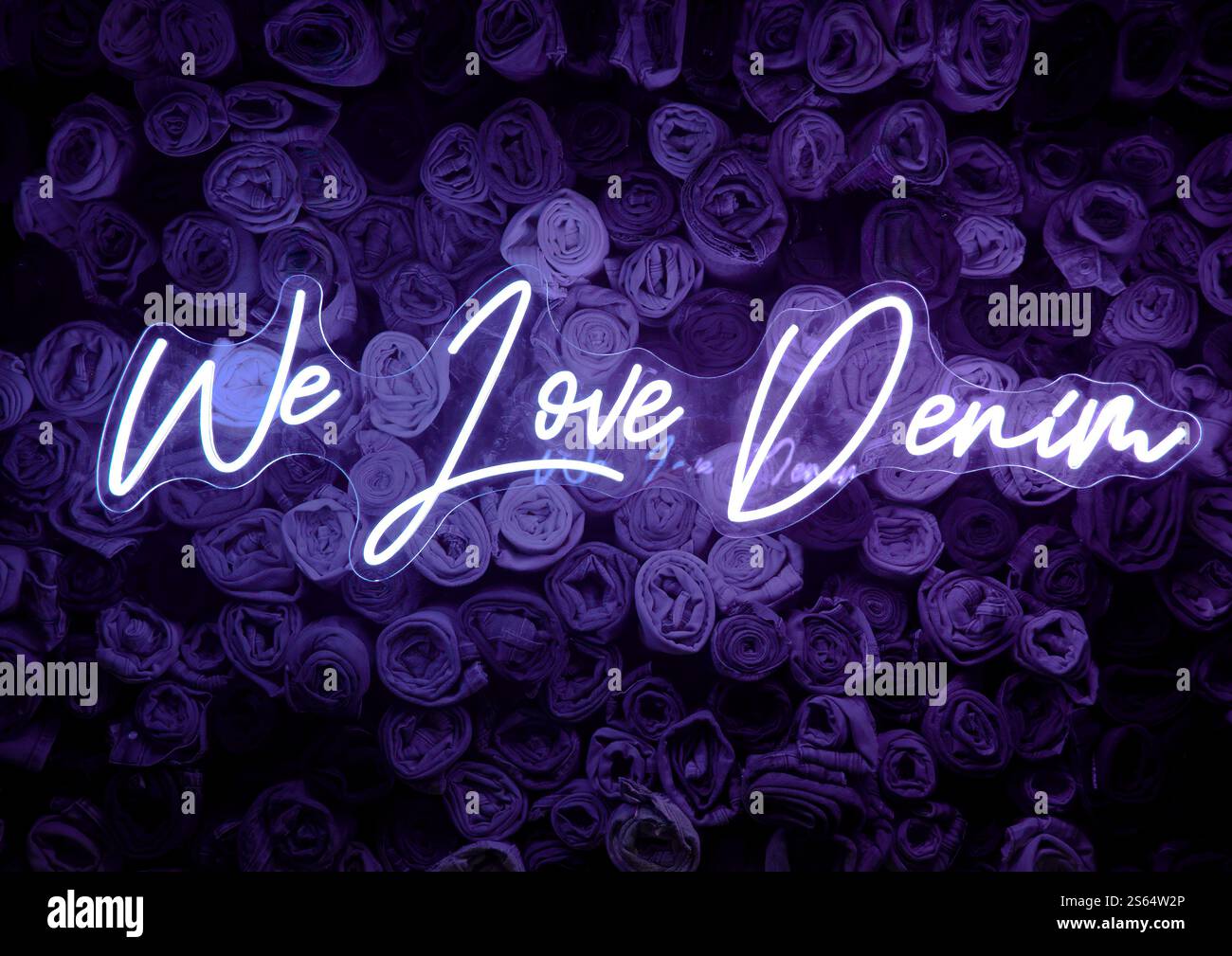 Insegna al neon viola "We Love Denim" davanti allo sfondo dei jeans. Foto Stock