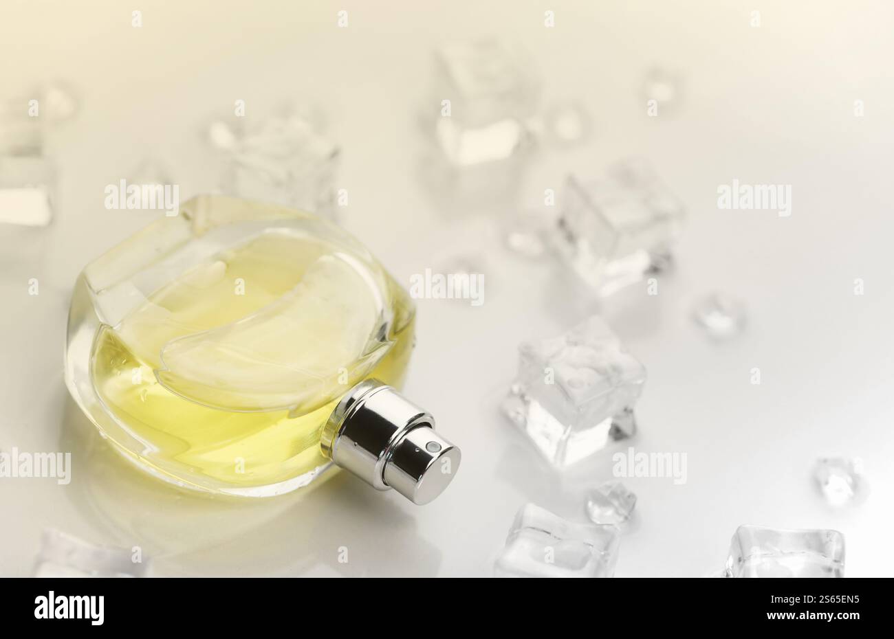 Bottiglia gialla di profumo femminile, fotografia obiettivo della bottiglia di profumo in cubetti di ghiaccio e acqua su un tavolo bianco. Vista dall'alto. Foto del prodotto mockup, Foto Stock