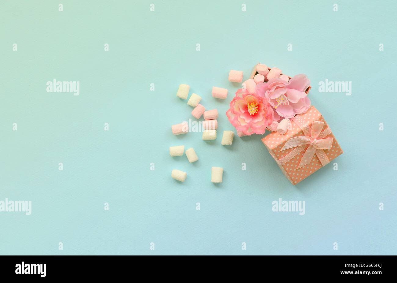 Confezione regalo rosa fiorita cosparsa di marshmallow su sfondo blu. Concetto metaforico lavorazione e coltivazione di fiori. Minimalismo piatto Foto Stock