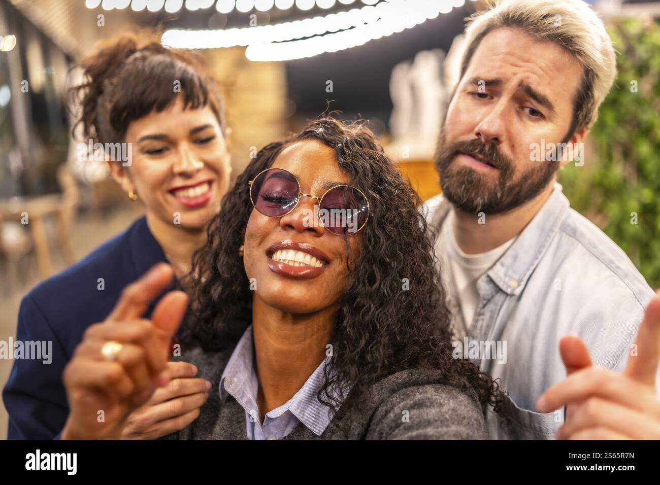 Primo piano e punto di vista personale di amici multietnici che tirano volti divertenti mentre scattano selfie in una festa notturna all'aperto Foto Stock