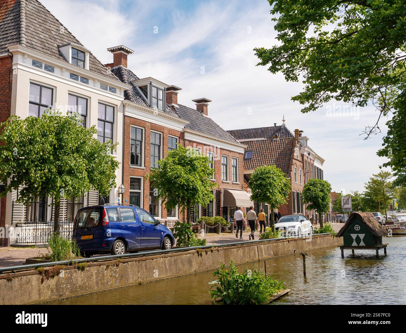 Persone che camminano lungo la strada Turfmarkt lungo il canale nella storica città vecchia di Makkum, Frisia, Paesi Bassi Foto Stock