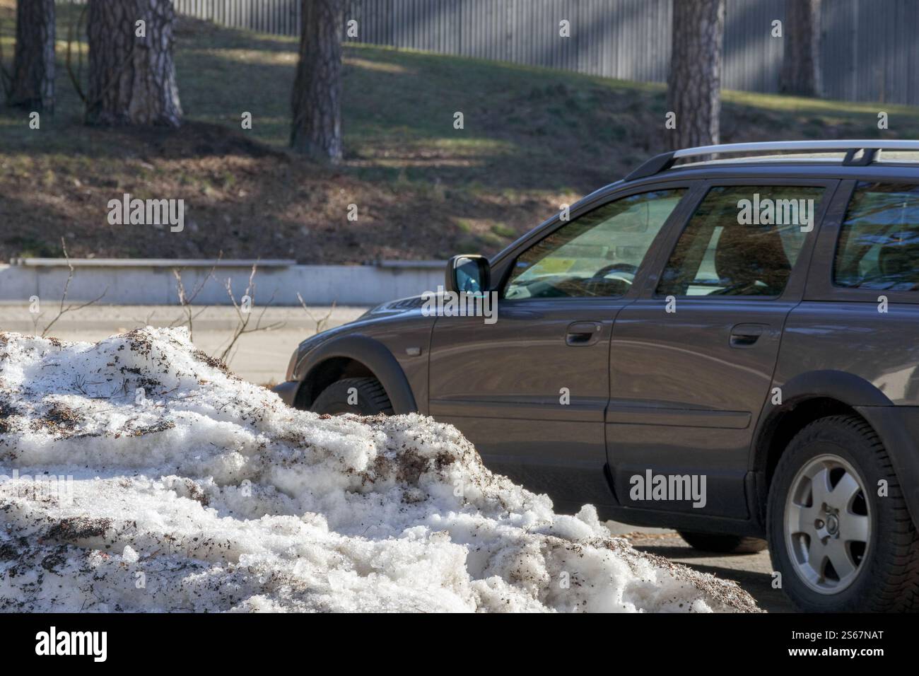 Incrocio grigio scuro che guida su una strada innevata oltre gli alberi. Foto Stock