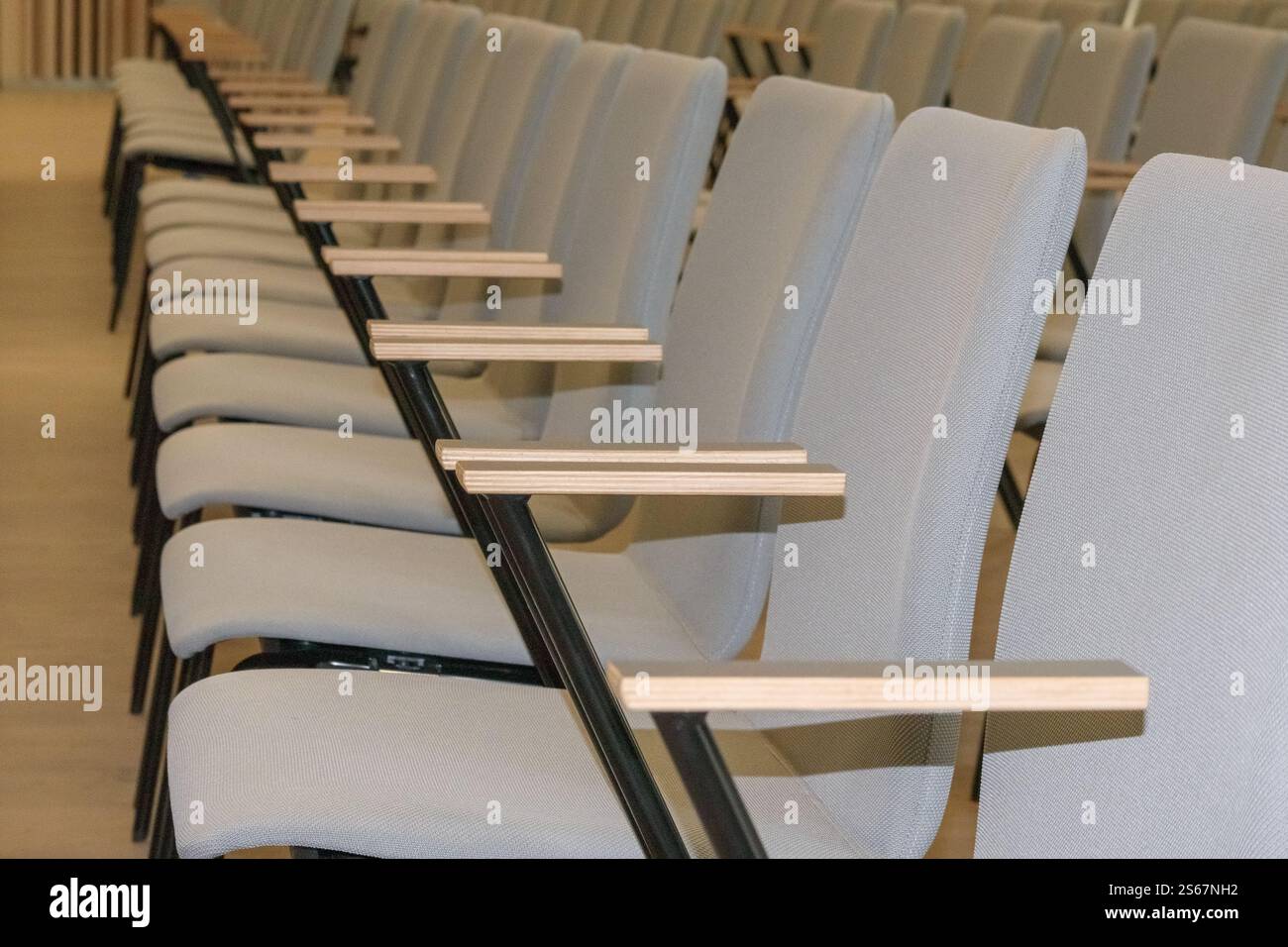 Frammento vuoto di una sala conferenze o di un auditorium con file di sedie grigie con bracci di legno. Foto Stock