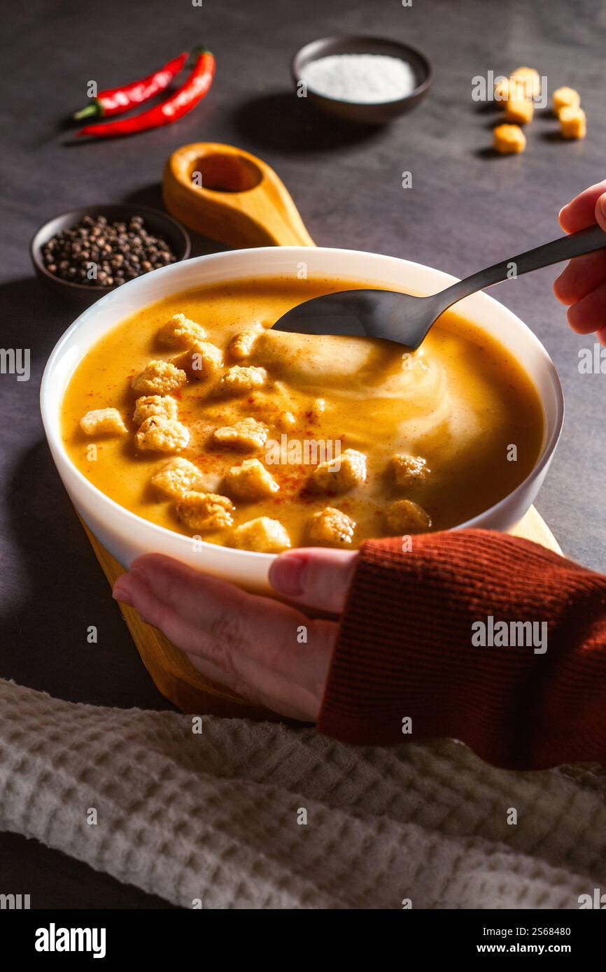 Donna che assaggia zuppa di zucca con cucchiaio. Mangiare zuppa di panna. Angolo alto. Tavolo servito con recipiente per zuppe, pepe, peperoncino, sale. Foto Stock