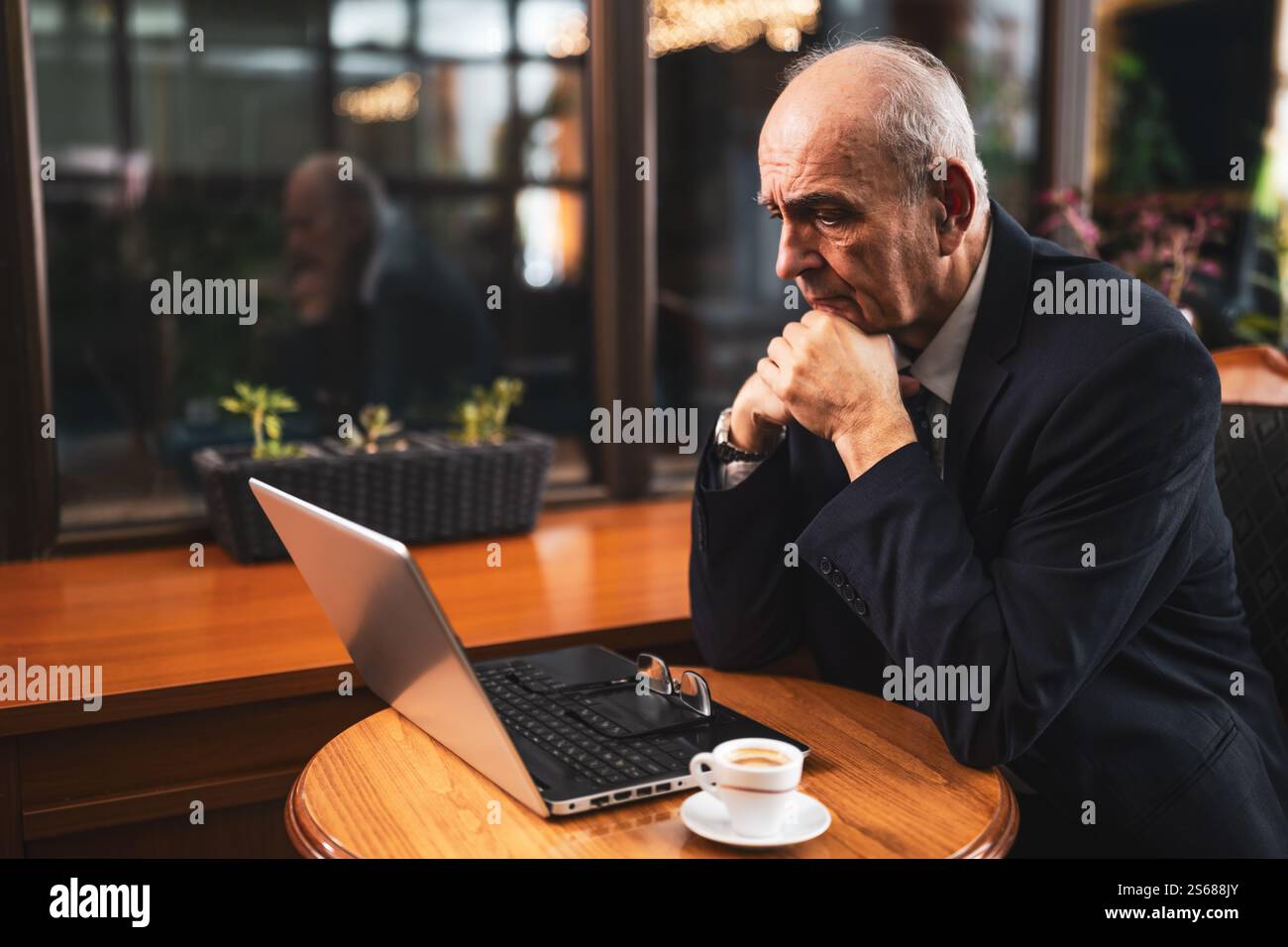 Un uomo d'affari anziano che lavorava troppo in costume e usava un computer portatile mentre lavorava e beveva un caffè nel caffè della città. Foto Stock