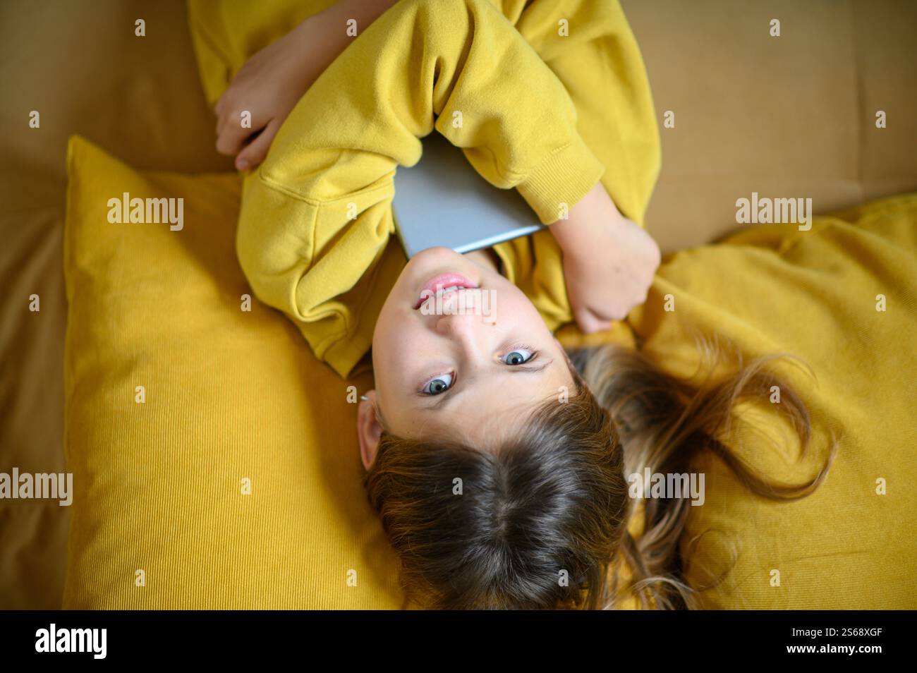 Una ragazza sdraiata, abbraccia il suo tablet con un'espressione gioiosa, irradia felicità ed eccitazione in un momento accogliente e rilassato. Foto Stock