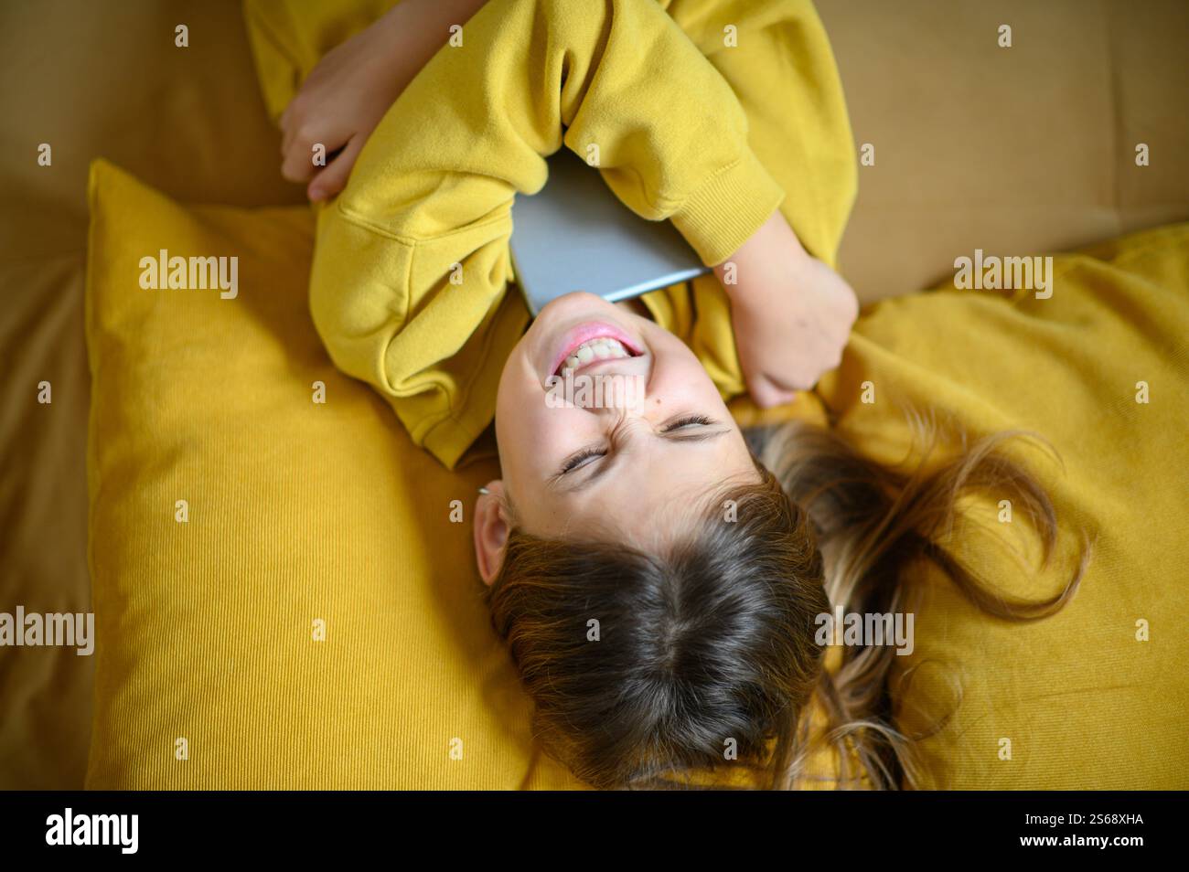 Una ragazza sdraiata, abbraccia il suo tablet con un'espressione gioiosa, irradia felicità ed eccitazione in un momento accogliente e rilassato. Foto Stock