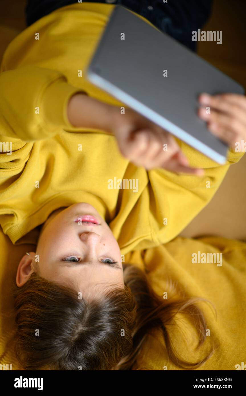 Una ragazza sdraiata, abbraccia il suo tablet con un'espressione gioiosa, irradia felicità ed eccitazione in un momento accogliente e rilassato. Foto Stock