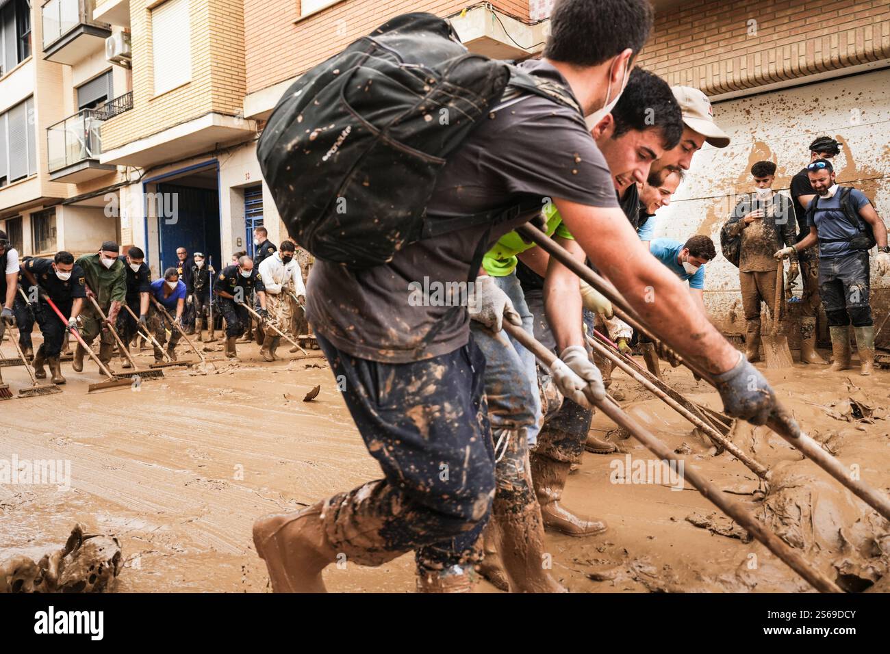 Volontari in due linee con spazzole spazzatrici che lavorano insieme spazzando fango dalle strade nelle inondazioni DANA. Massanassa, Spagna 2. Foto Stock