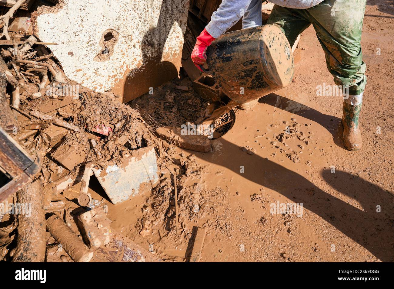 Persona irriconoscibile che getta fango da un secchio a un tombino e fognature. Backlog fognario intasato di fango. Foto Stock