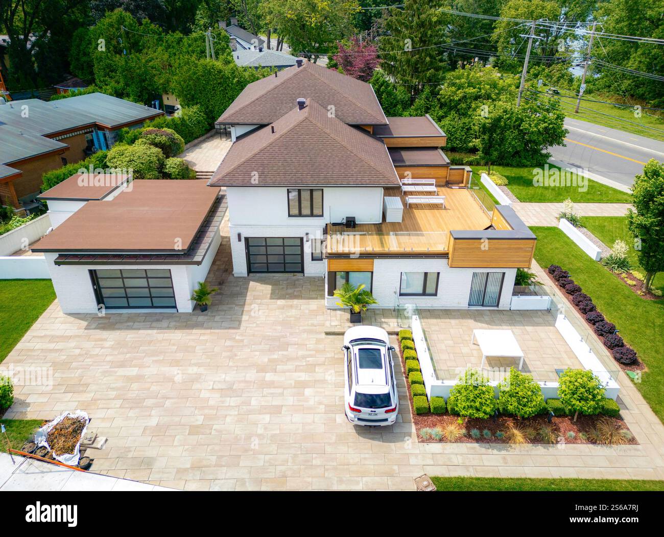 Una moderna casa di lusso con un ampio vialetto, architettura contemporanea, design a tetto piatto e verde paesaggistico, circondato da alberi Foto Stock