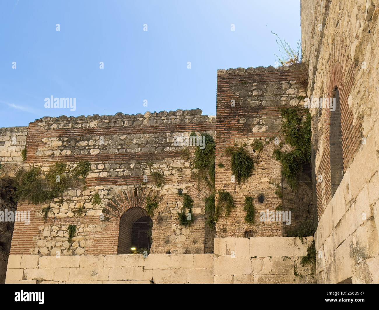 Spalato, Croazia - 1° luglio 2024: Storiche cantine e palazzo di Diocleziano. Livelli superiori con piante che crescono in crepe delle pareti sotto il cielo blu Foto Stock Spalato, Croazia - 1° luglio 2024: Storiche cantine e palazzo di Diocleziano. Livelli superiori con piante che crescono in crepe delle pareti sotto il cielo blu Foto Stock