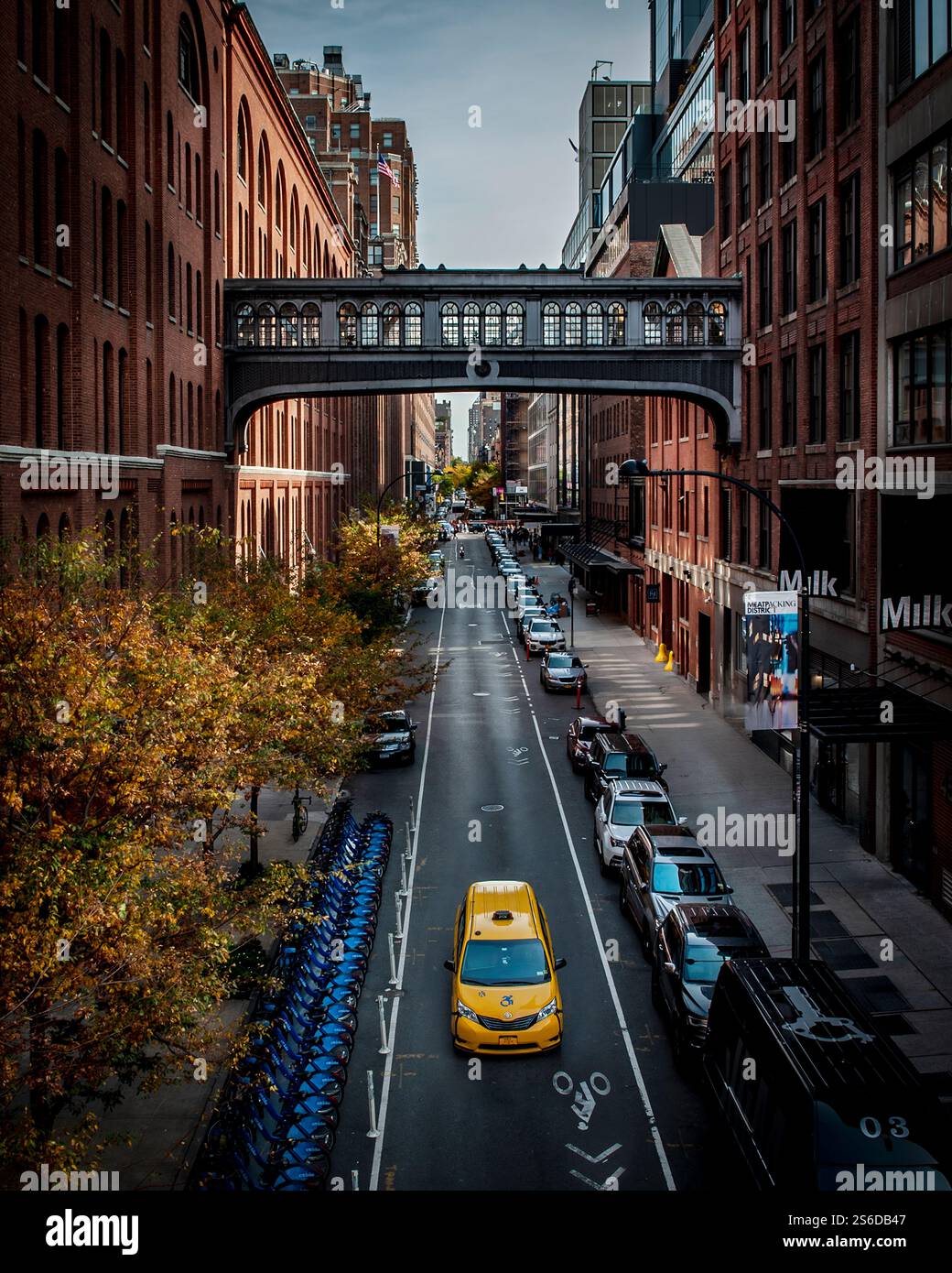 Il taxi giallo attraversa West 15th Street, incorniciato da edifici in mattoni rossi e dal ponte al Chelsea Market. Catturato da Highline Park, un vero momento di New York. Foto Stock