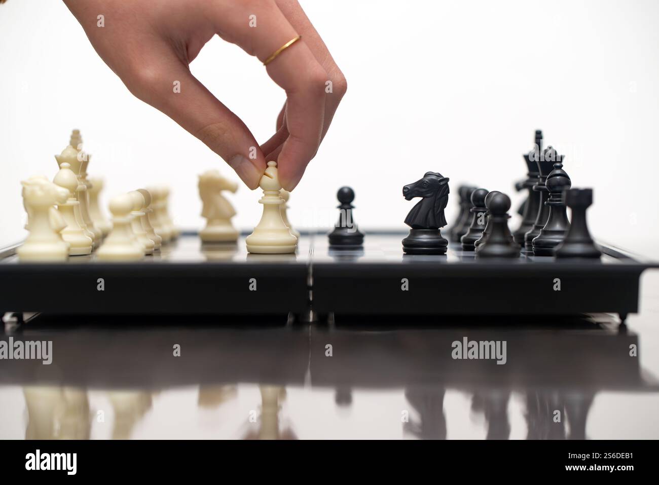 Primo piano di una scacchiera che mostra una mano che muove una regina bianca, catturando l'essenza strategica del gioco. I pezzi da scacchi in bianco e nero sono pronti per giocare. Foto Stock