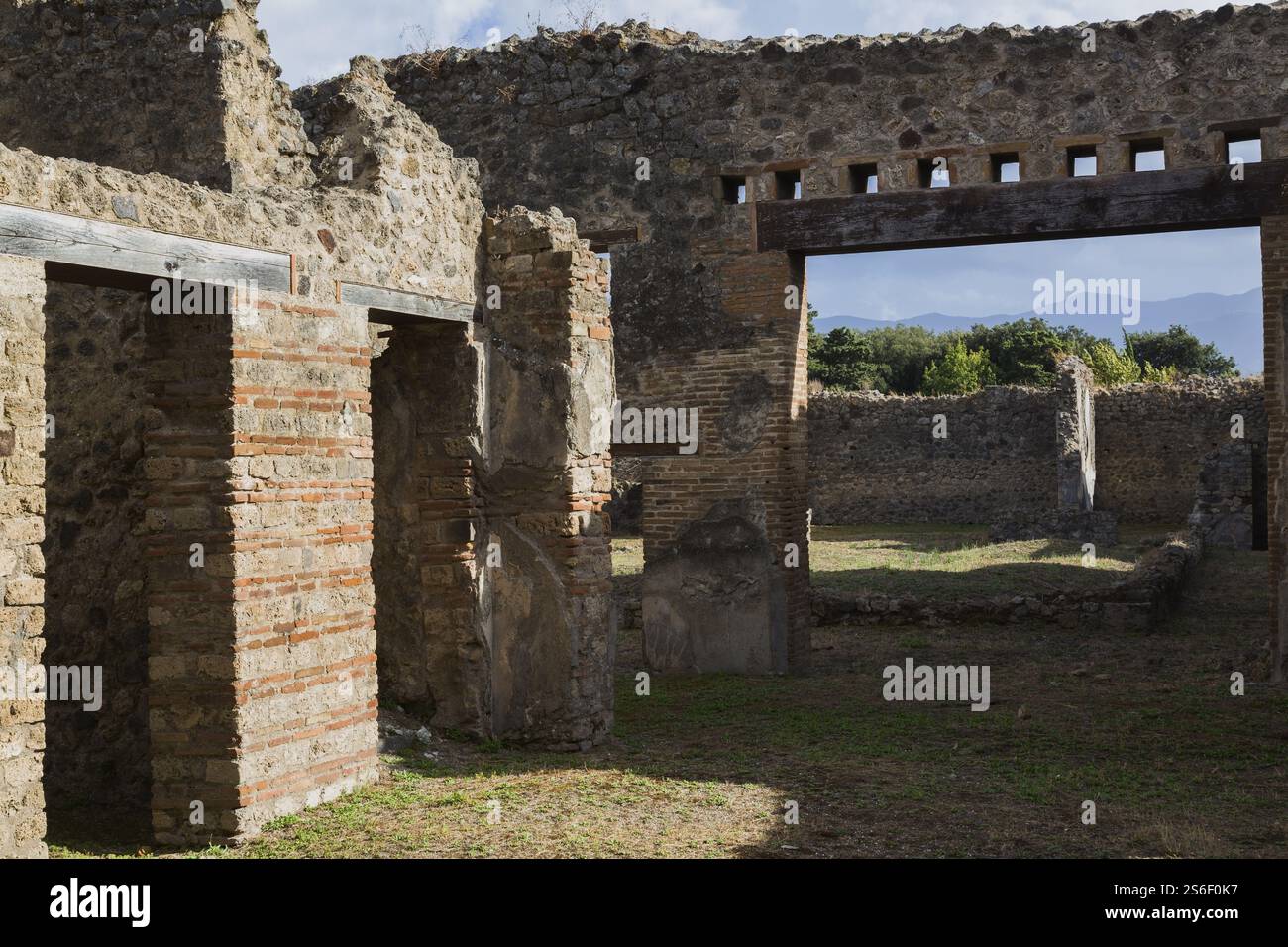 Porte di edifici residenziali e grande apertura in resti di vecchie strutture murarie in mattoni e pietre di terracotta più cortile con terreno marrone Foto Stock