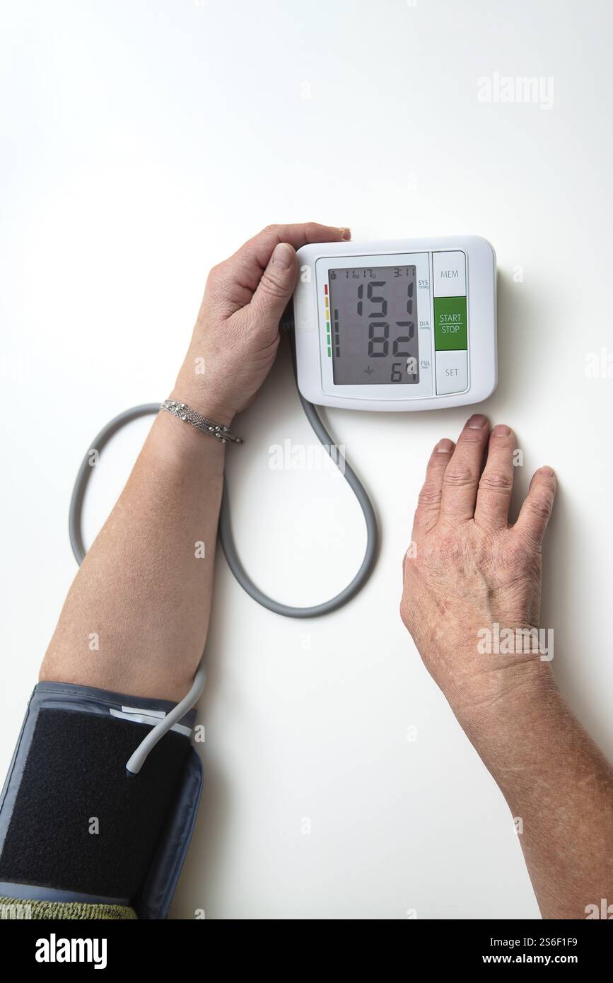 Mani di una donna adulta anziana che utilizza un misuratore di pressione sanguigna portatile, controllando la sua salute a casa Foto Stock
