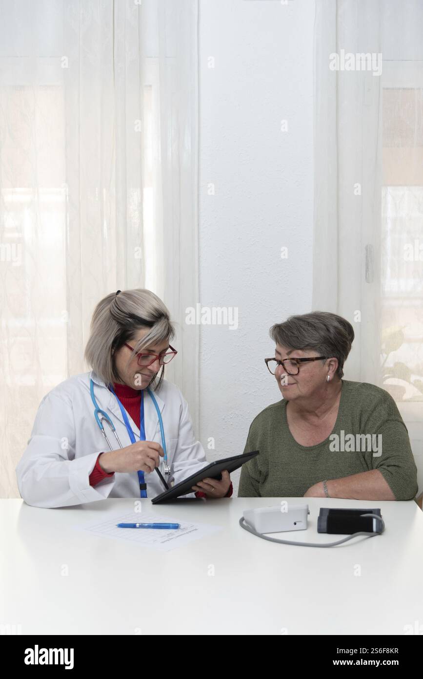 Medico che mostra informazioni mediche su tablet digitale al paziente anziano durante la visita a casa, fornendo assistenza sanitaria e supporto personalizzati Foto Stock