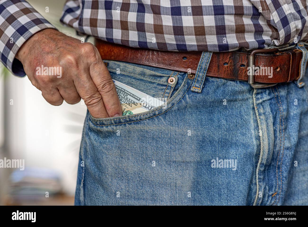 Il punto è il denaro: Primo piano della mano di un uomo che lancia un pacchetto di banconote da cento dollari americane nella tasca anteriore dei suoi jeans. Foto Stock