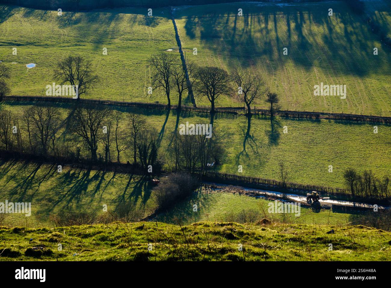 Un trattore che percorre una strada di campagna nel tardo pomeriggio con il sole invernale, nella parte superiore della dove Valley vicino a Crowdecote, al Peak District National Park, Derbyshire Foto Stock