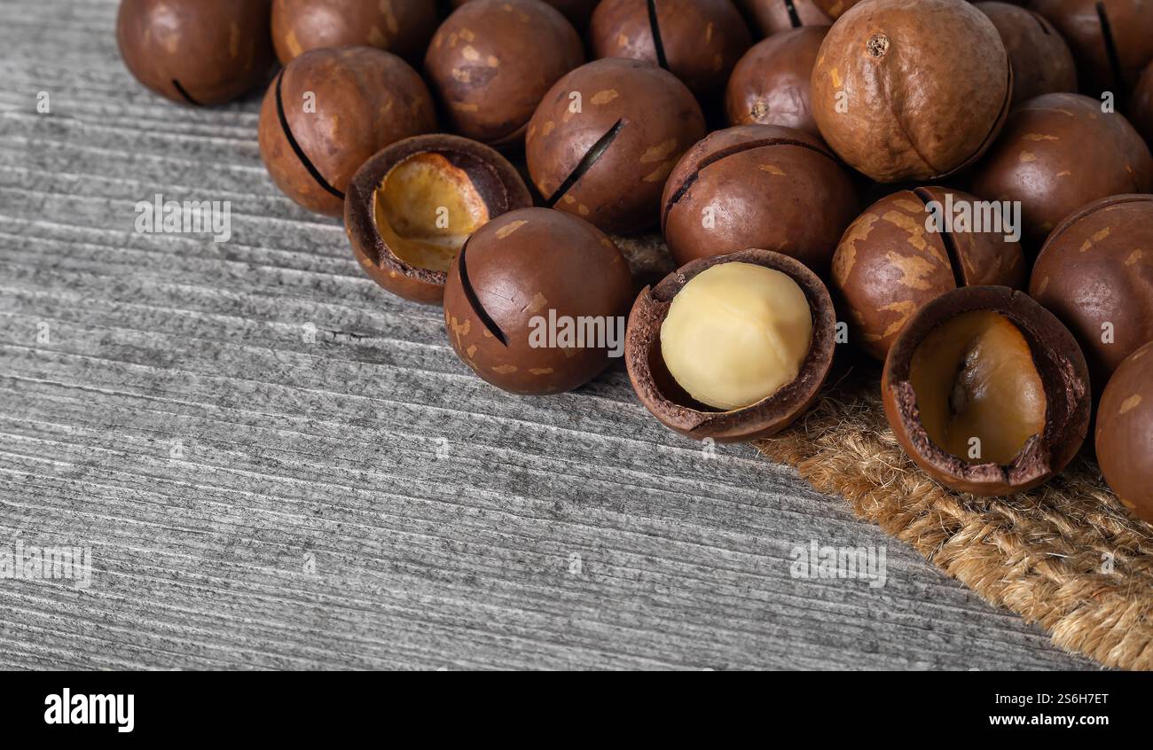 Le noci di macadamia in gusci fessurati sono disposte ordinatamente su una superficie rustica in legno, che mostra il loro ricco colore e consistenza marrone. Foto Stock