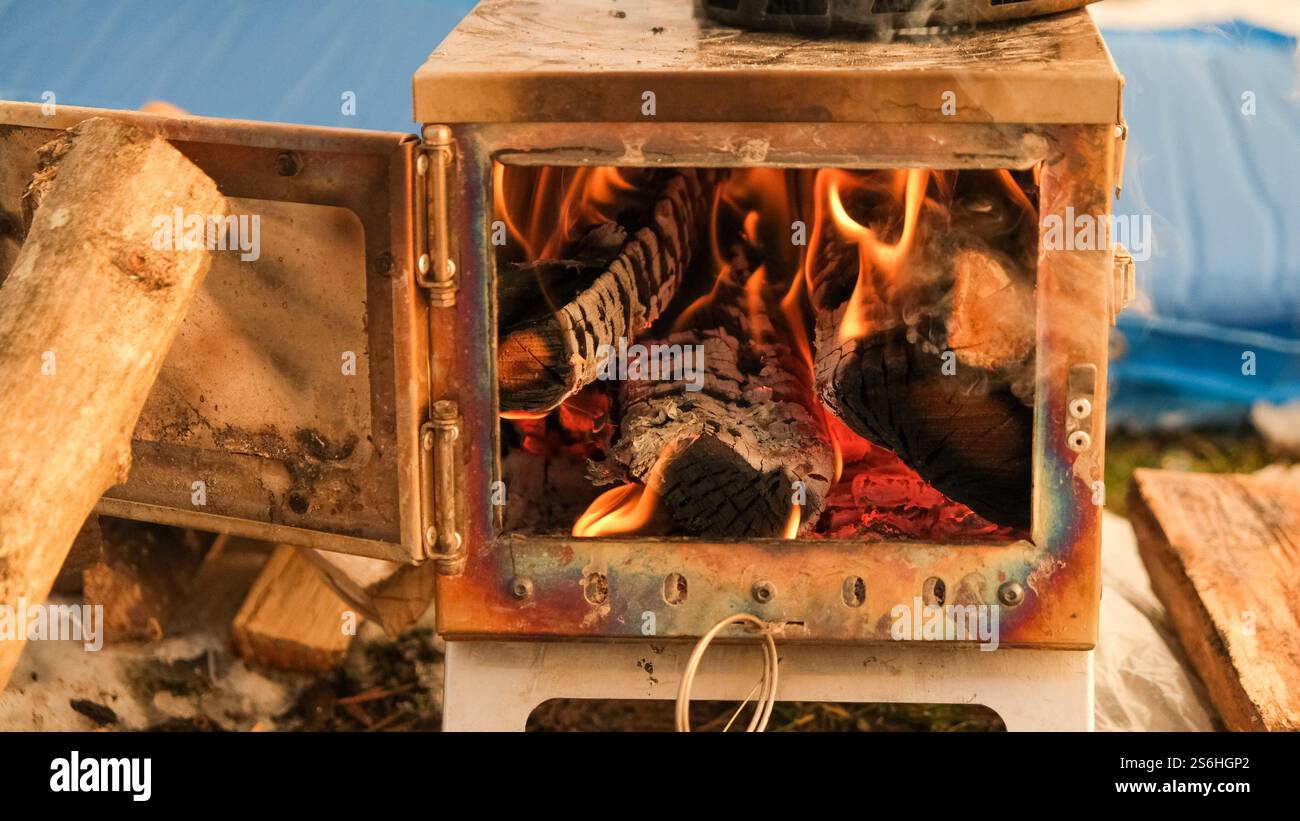 Una stufa a legna aperta in una tenda da campeggio, che irradia calore. La stufa è piena di legna da ardere, creando un'atmosfera accogliente per il campeggio invernale. Foto Stock