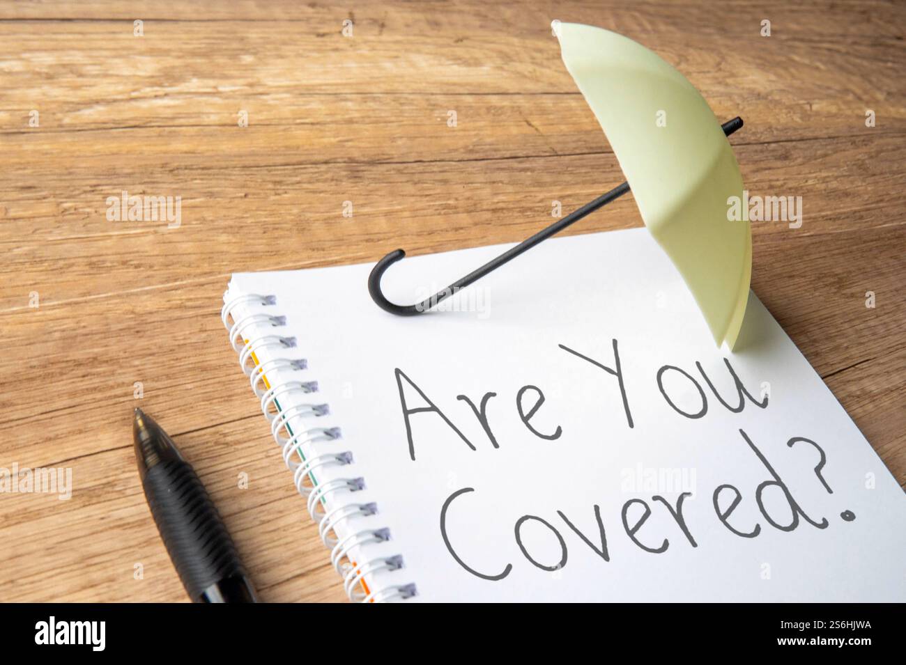 Un piccolo ombrello è posizionato sopra un notebook con le parole "sei coperto?". Concetto di protezione, assicurazione, sicurezza finanziaria. Foto Stock