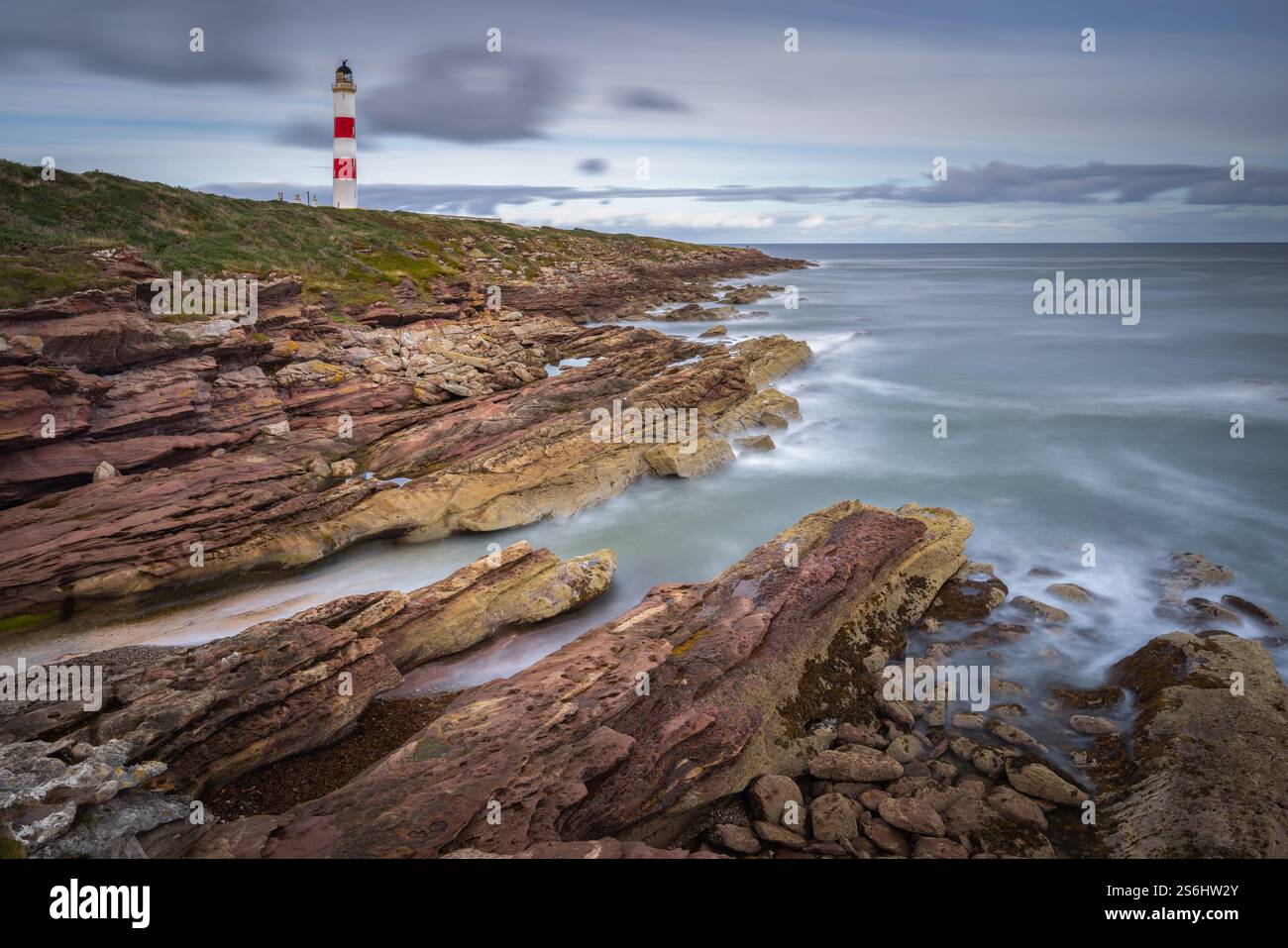 Onde che si infrangono sulle rocce a Wilkhaven Point con il faro di Tarbatness sullo sfondo, in Scozia Foto Stock