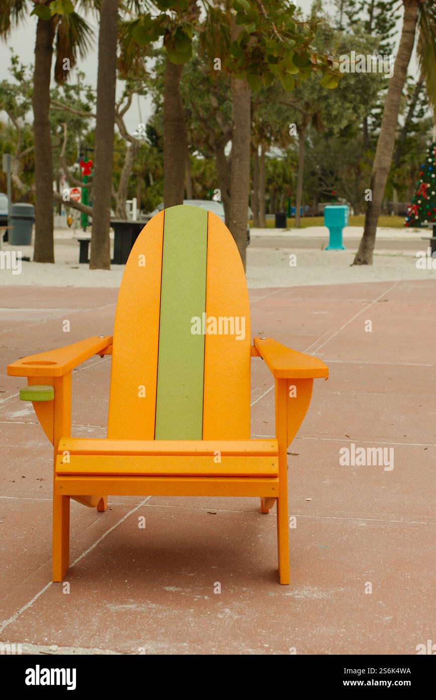 Sedia Adirondack verde e arancione isolata sul padiglione che si affaccia sul Golfo del Messico a St. Pete Beach, Florida . Vista dalla spiaggia Pass-a-Grille. Palmo Foto Stock