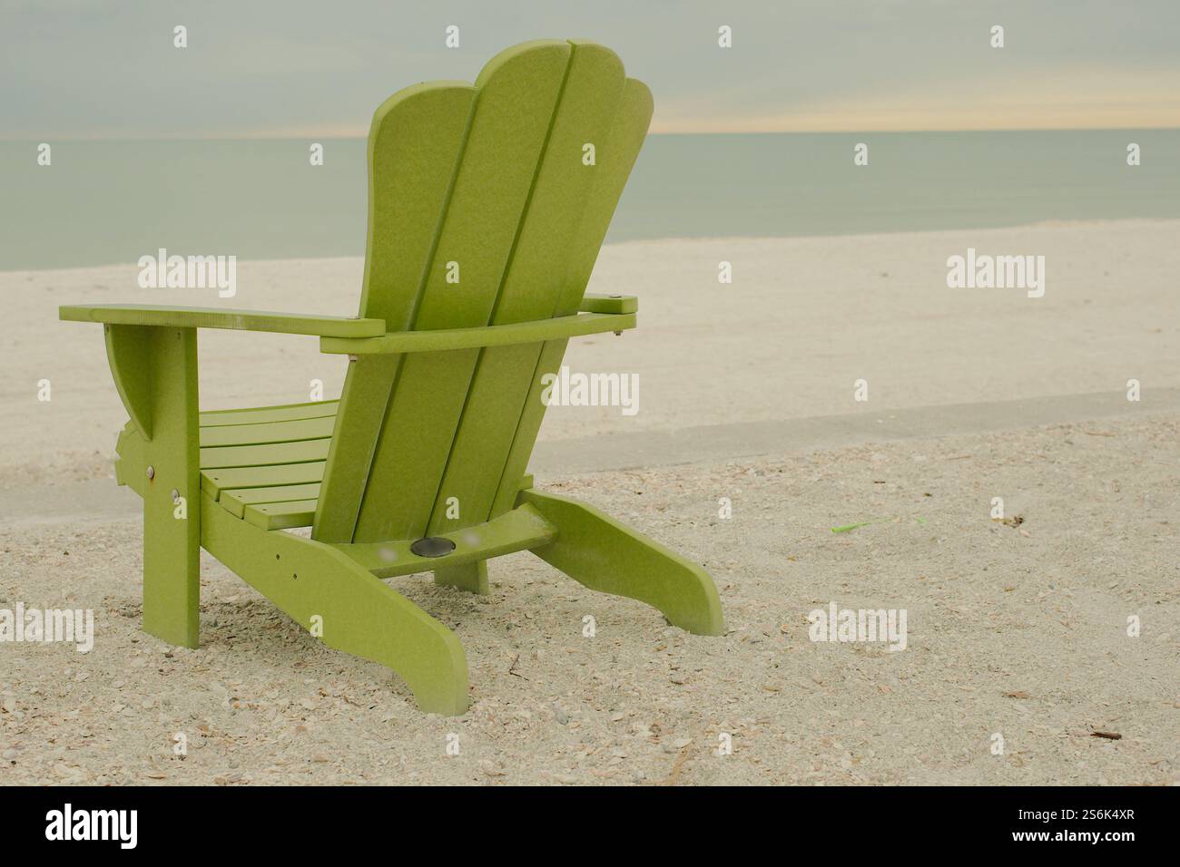 Sedia verde isolata Adirondack di fronte al Golfo del Messico a St. Pete Beach, Florida . Vista dalla spiaggia di Pass-a-Grille sulla sabbia in una giornata nuvolosa. Foto Stock