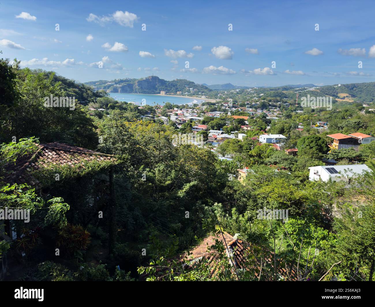 La splendida vista mostra la città costiera annidata tra alberi con cieli azzurri e montagne lontane. Foto Stock