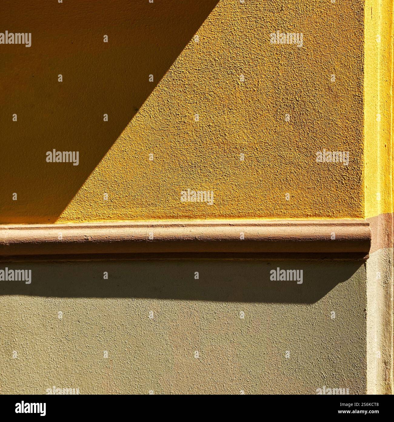 Composizione minimalista che mostra una parete illuminata dal sole con vivaci tonalità giallo e beige, evidenziando forme geometriche e superfici testurizzate Foto Stock