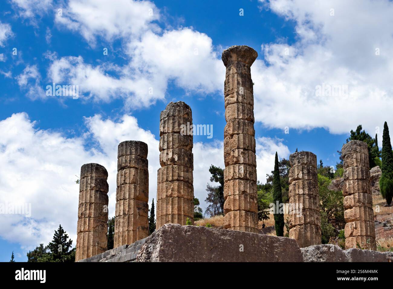Antiche colonne in pietra del Tempio di Apollo a Delfi, Grecia, che si innalzano sotto un cielo blu luminoso con nuvole sparse. Foto Stock