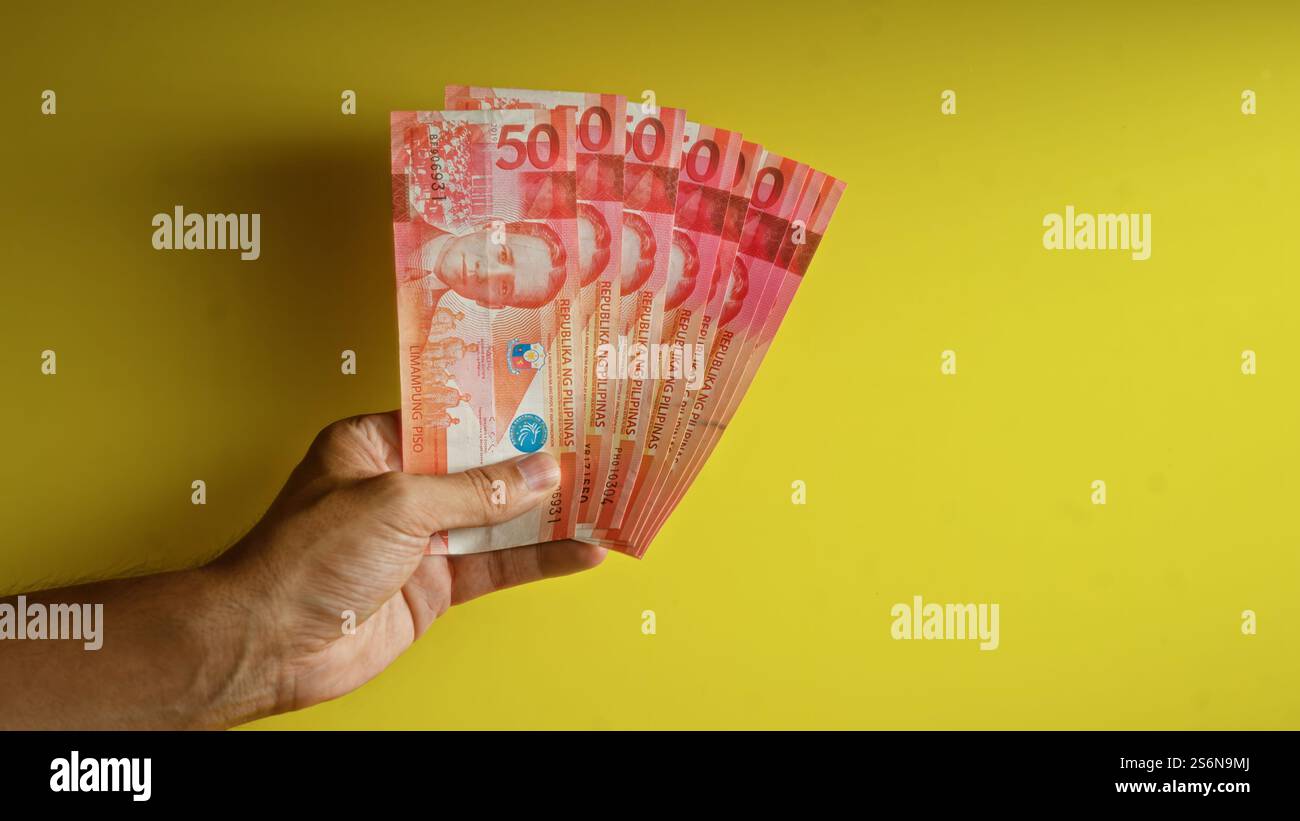 Mano che regge più banconote in peso filippino su un vivace sfondo giallo che dimostra ricchezza e concetto finanziario Foto Stock