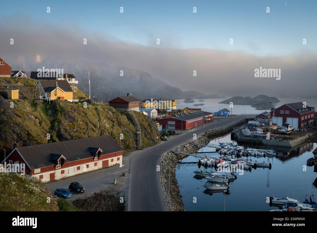 La città di Sisimiut mostra il suo fascino con case colorate e acque tranquille alla luce del mattino presto, invitando a esplorare il porto panoramico. Foto Stock