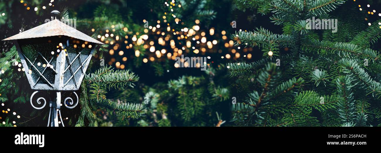 Rami di abete con lanterna e luci bokeh intemprate. Sfondo natalizio orizzontale con un caldo bagliore e spazio per il testo. Foto Stock