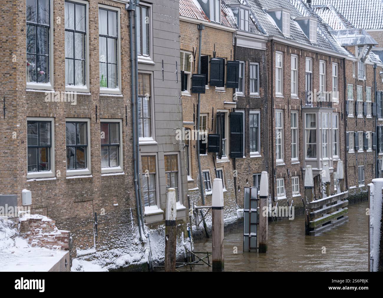 Una fila di vecchi e tortuosi edifici olandesi ricoperti di neve si affaccia su un canale. L'ambiente invernale cattura l'architettura e la bellezza pacifica Foto Stock