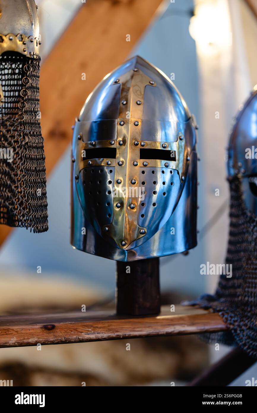 Un casco argentato con una croce è esposto su una mensola di legno. L'elmetto è circondato da una recinzione a catena, che gli dà la sensazione di essere in displ Foto Stock