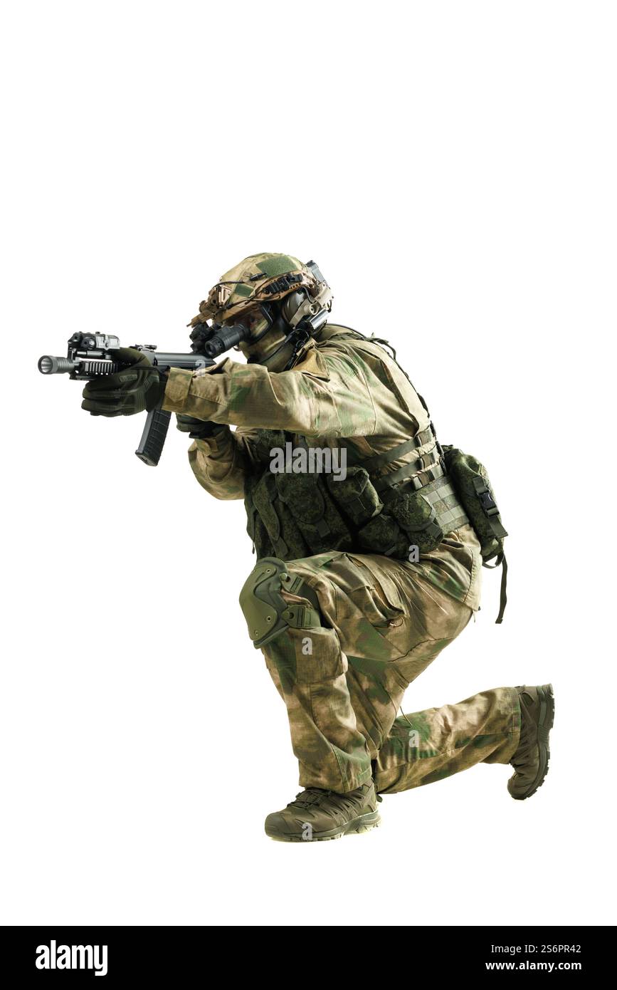 Un soldato vestito con equipaggiamento mimetico completo, che punta un fucile mentre si inginocchia. Immagine che raffigura la preparazione alle operazioni militari tattiche e la prontezza al combattimento, Foto Stock