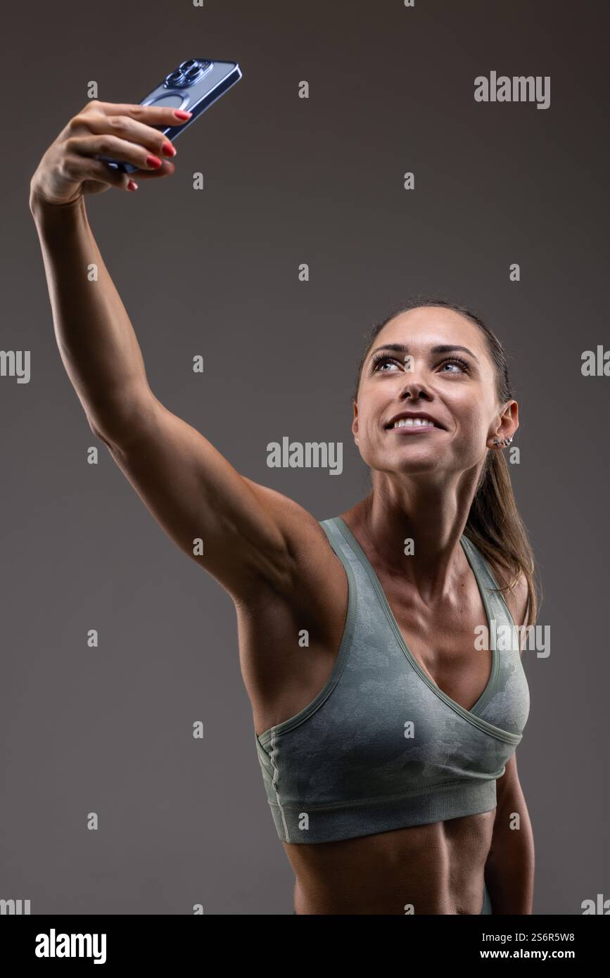 Una donna in vestibilità atletica che cattura un selfie, trasudando fiducia e positività. Il dispositivo moderno e la sua energia vibrante enfatizzano la vita fisica Foto Stock