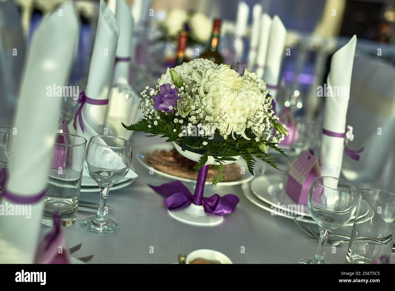 Formale tavolo da pranzo decorato con un centrotavola floreale, tovaglioli bianchi legati con nastri viola e bicchieri per un ambiente elegante e decorato per eventi Foto Stock