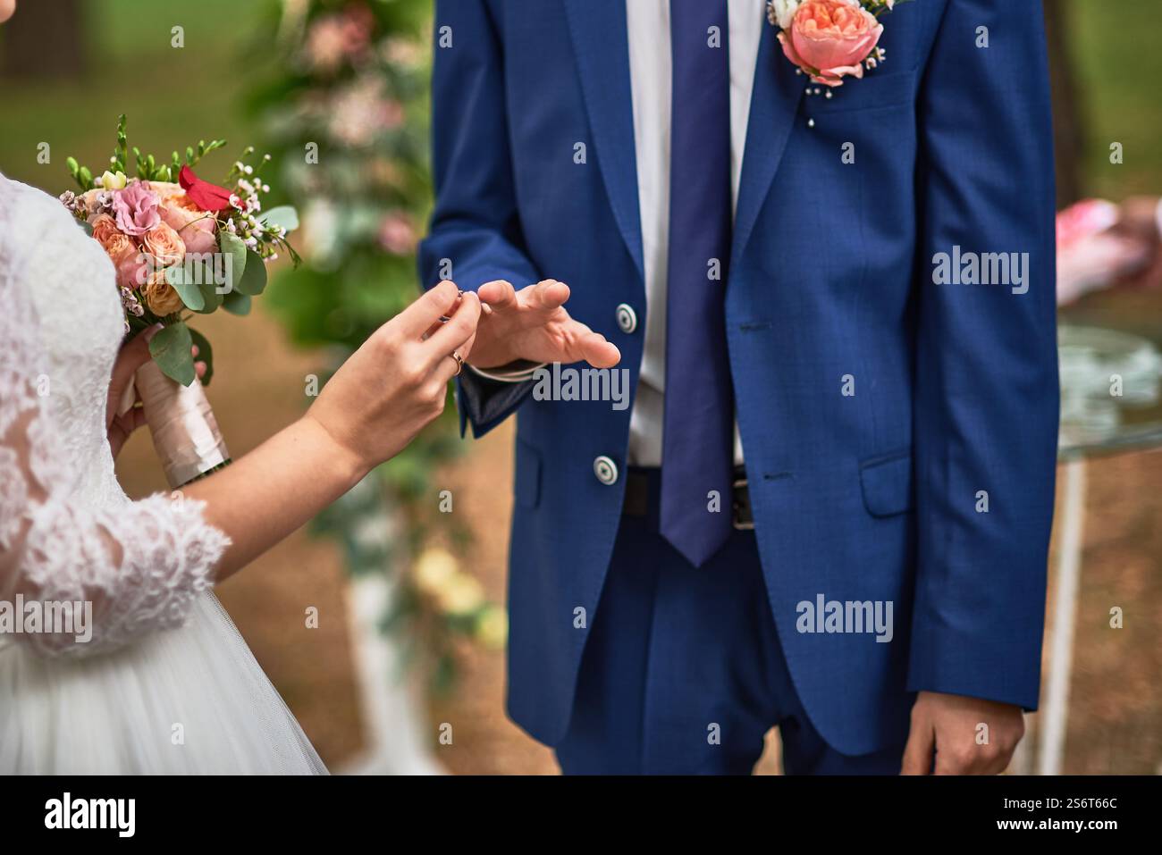 Sposa e sposo si scambiano le fedi nuziali, un momento simbolico d'amore, in una romantica cerimonia all'aperto, vestita con abiti da sposa, adornata da una splendida Foto Stock