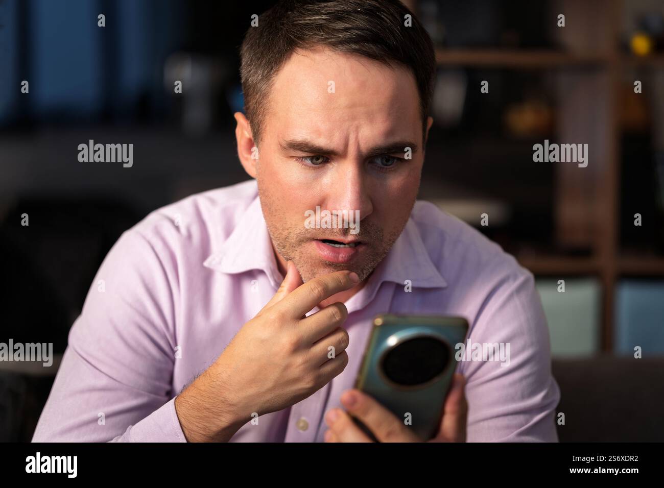 un uomo che scrive sullo smartphone di casa e rimane scioccato. uomo usa il suo smartphone rosa. Scioccate cattive notizie Foto Stock
