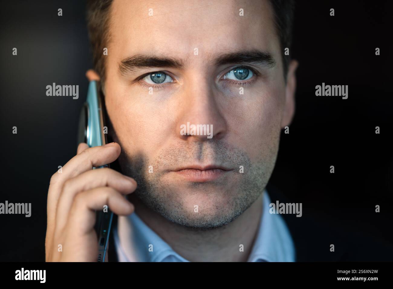 Giovane uomo d'affari che parla al telefono di notte nell'ufficio moderno. primo piano della faccia di un giovane che parla al telefono con uno sfondo scuro di notte. Foto Stock