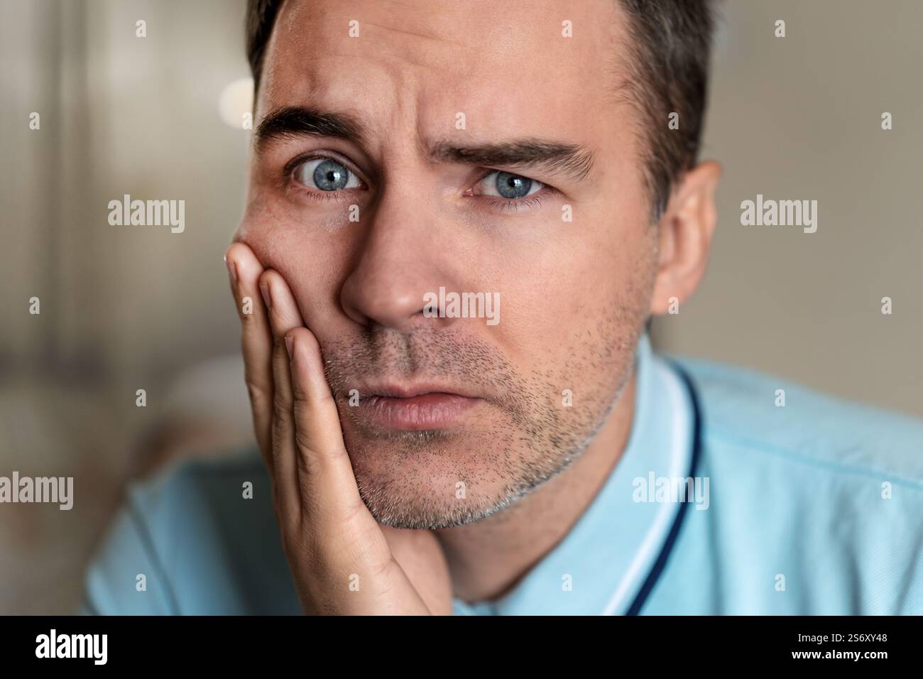 Una giovane con una triste emozione sul viso che tiene la mano sulla mascella della paziente su uno sfondo grigio. Ritratto di un uomo con espressione dolorosa Foto Stock