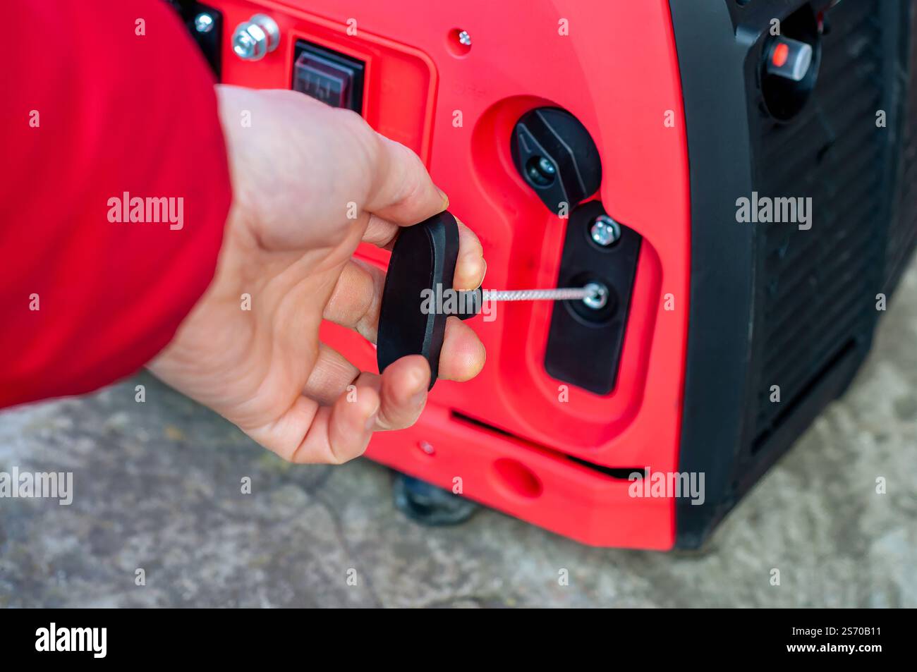 Tirare a mano la fune di avviamento di un generatore di benzina portatile rosso, pronto per l'avviamento Foto Stock