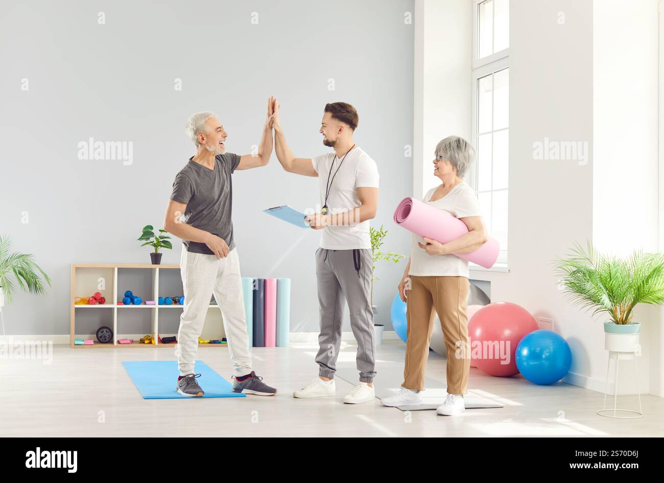 Gli anziani felici e attivi danno un alto cinque al loro istruttore di fitness in palestra Foto Stock
