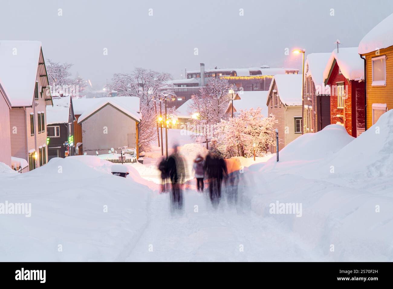 Strada innevata di Tromsø, Norvegia, durante la notte polare, persone che camminano in lontananza Foto Stock