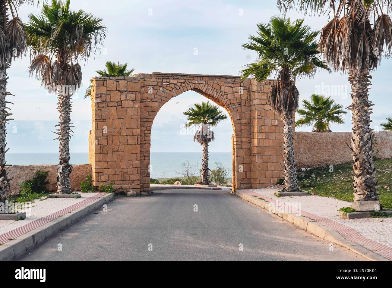 Pittoresca arcata in pietra a 'Oualidia' in Marocco con palme su entrambi i lati, che conduce ad una vista dell'oceano sullo sfondo. Foto Stock
